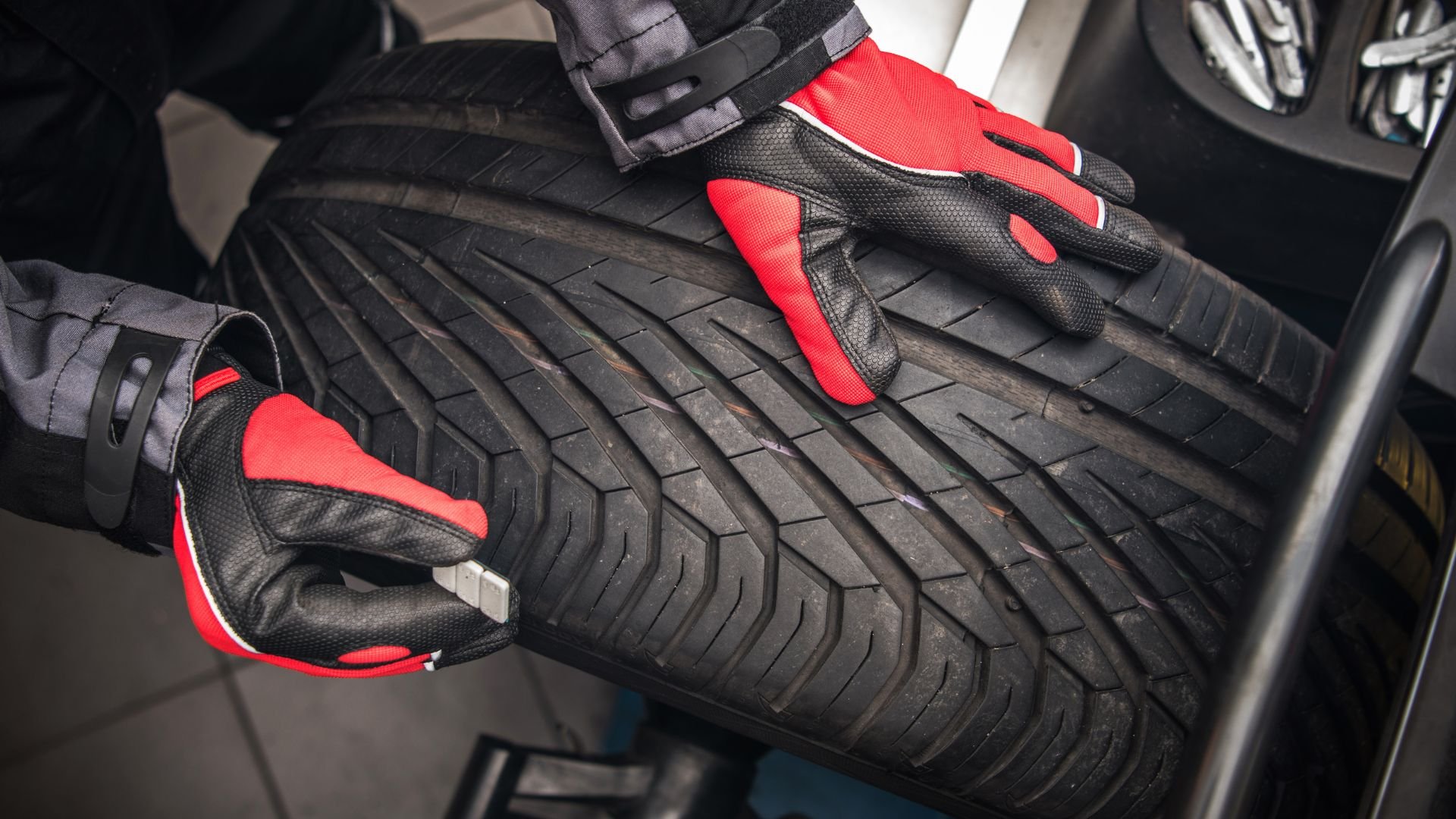 Hands in red and black gloves checking car tire tread