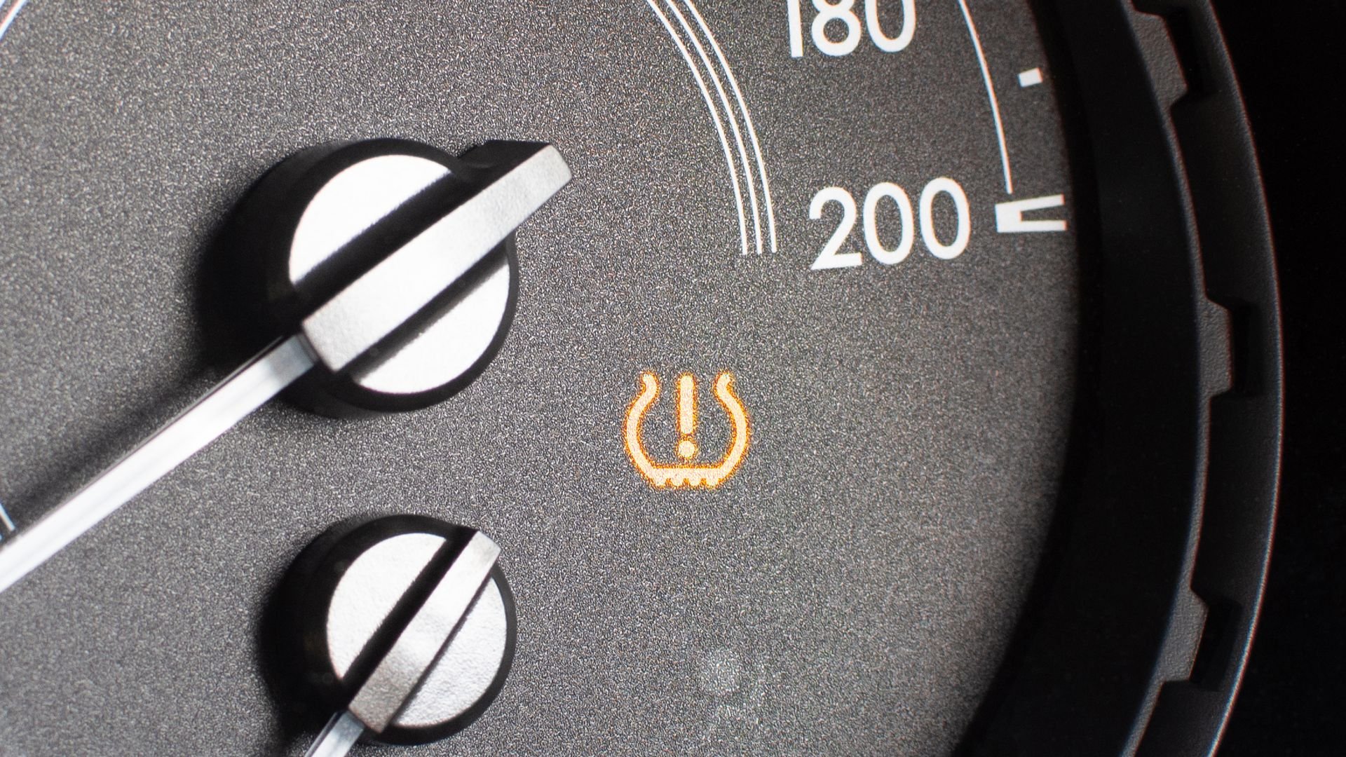 Tire pressure warning light illuminated on car dashboard near speedometer