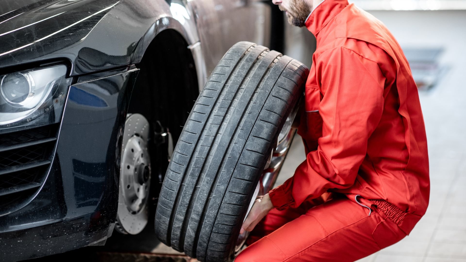 Mechanic in red uniform changing tire on black car in service garage