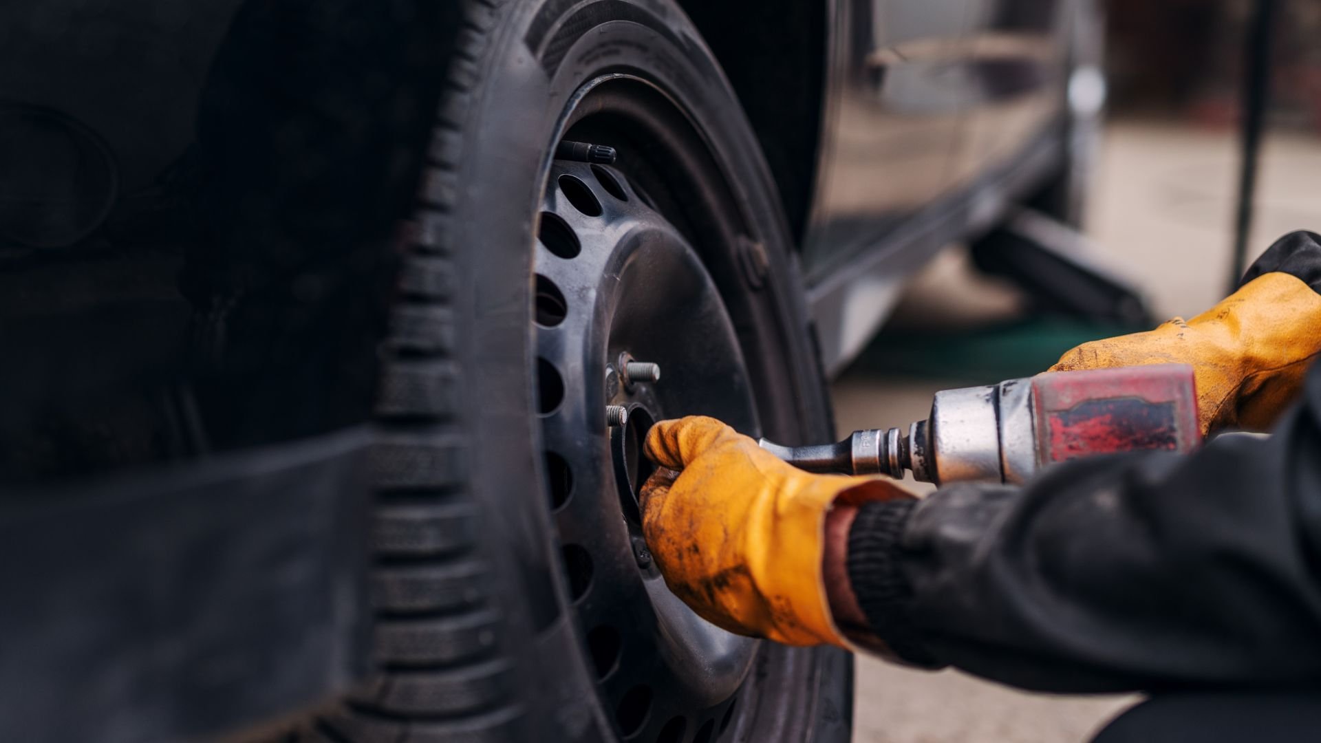 Mechanic uses power drill to change tire with yellow work gloves